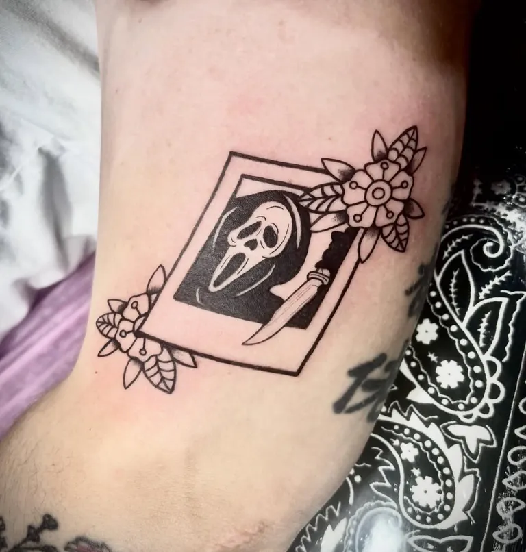 Ghost mask tattoo in a framed panel with flowers on the arm by Melissa at Golden Child Tattoo in Escondido