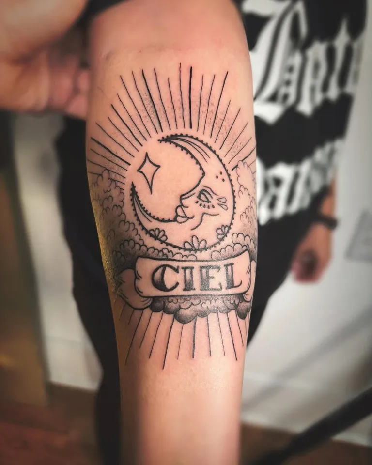 Crescent moon tattoo with a script banner on the forearm by Melissa at Golden Child Tattoo in Escondido