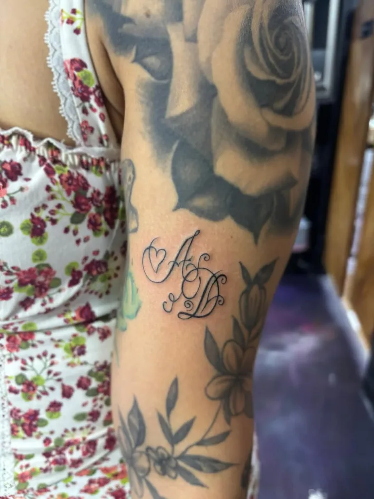 Script initials with a small heart, added among existing arm tattoos by Melissa at Golden Child Tattoo in Escondido