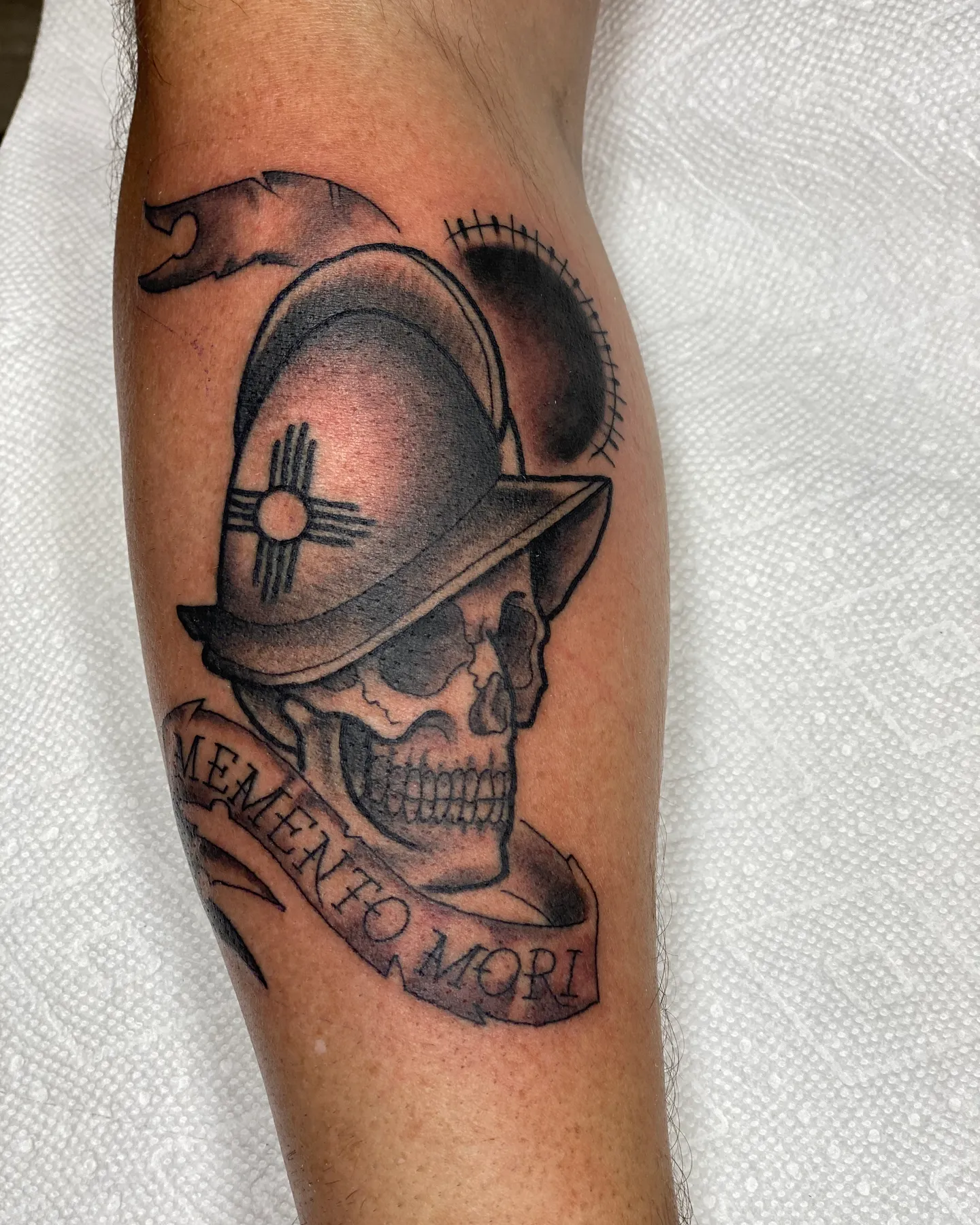 Black and grey skull in a conquistador helmet tattoo with a Memento Mori banner by Mathias Moretti at Golden Child Tattoo in Escondido