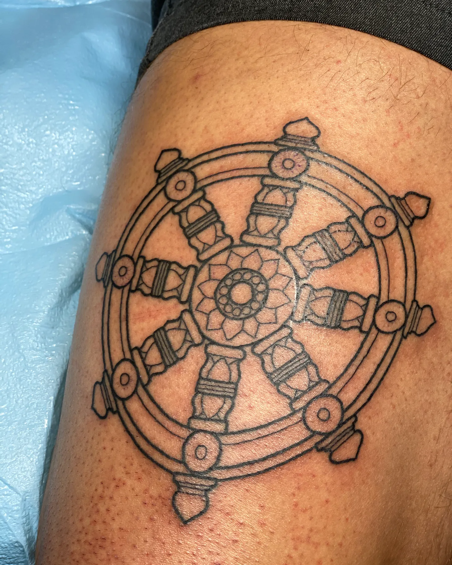 Black linework dharma wheel tattoo by Mathias Moretti at Golden Child Tattoo in Escondido