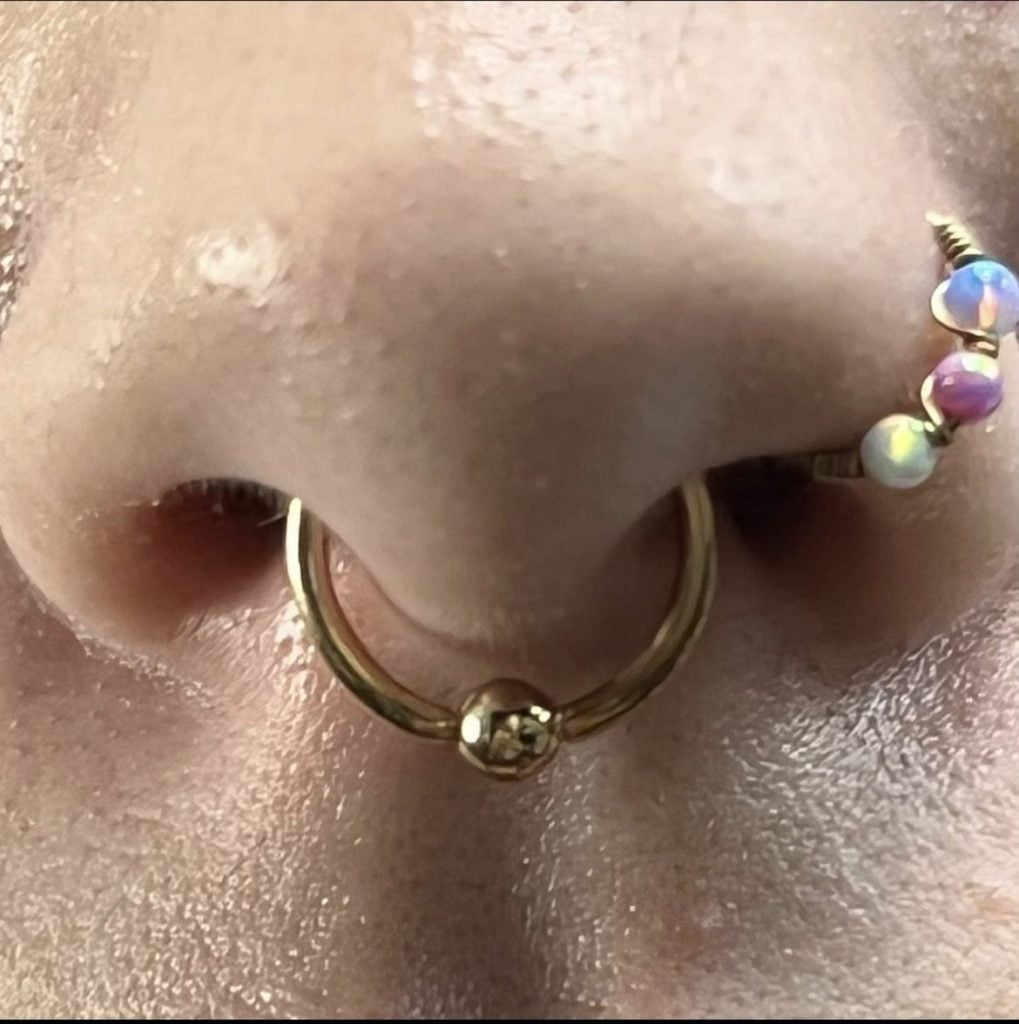 Close-up of a nose piercing with septum ring and colorful opal bead chain, by Birdie at Golden Child Tattoo and Piercing, Escondido