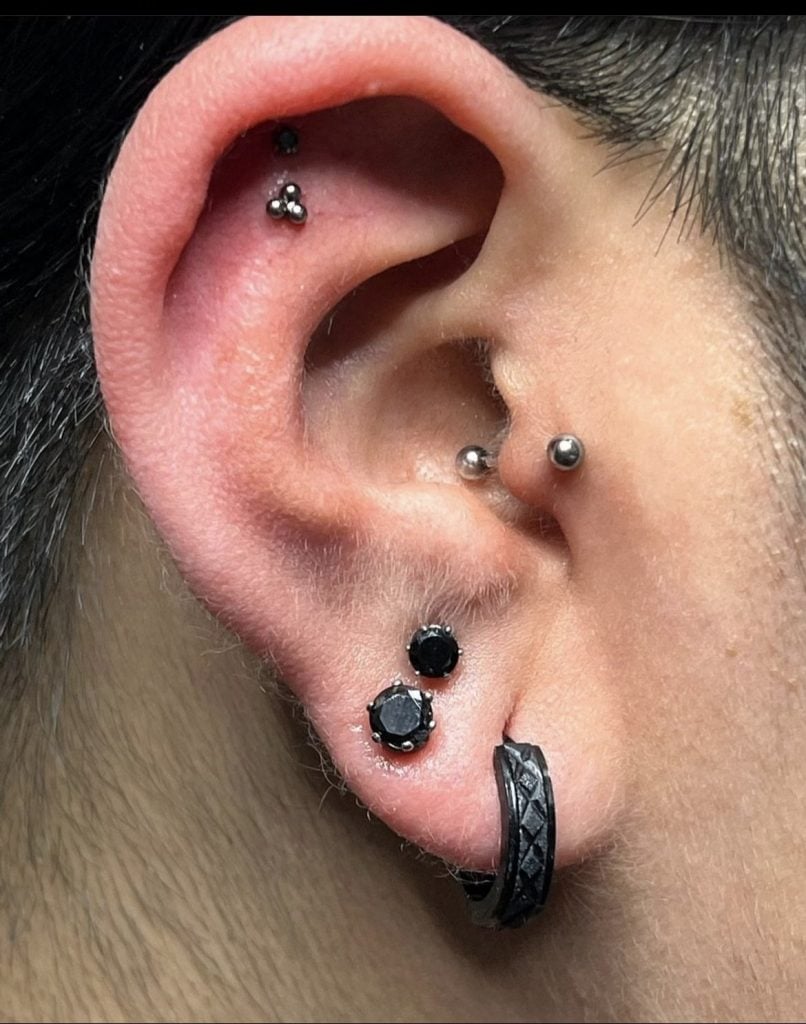 Multiple ear piercings including helix studs and a black woven hoop ring, by Birdie at Golden Child Tattoo and Piercing, Escondido