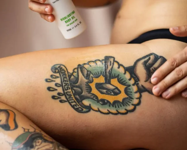 A close-up of a person's upper thigh featuring a bold, traditional-style tattoo with the text “Workers United.”